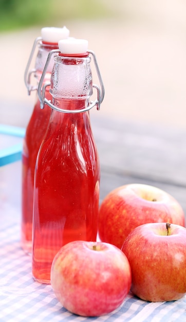 Botellas con bebidas rojas y algunas manzanas.