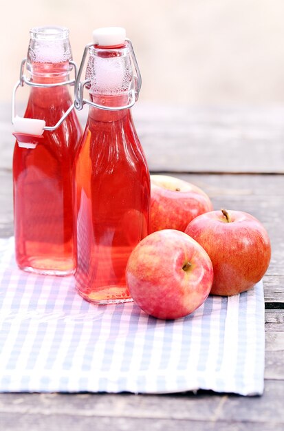 Foto gratuita botellas con bebidas rojas y algunas manzanas.