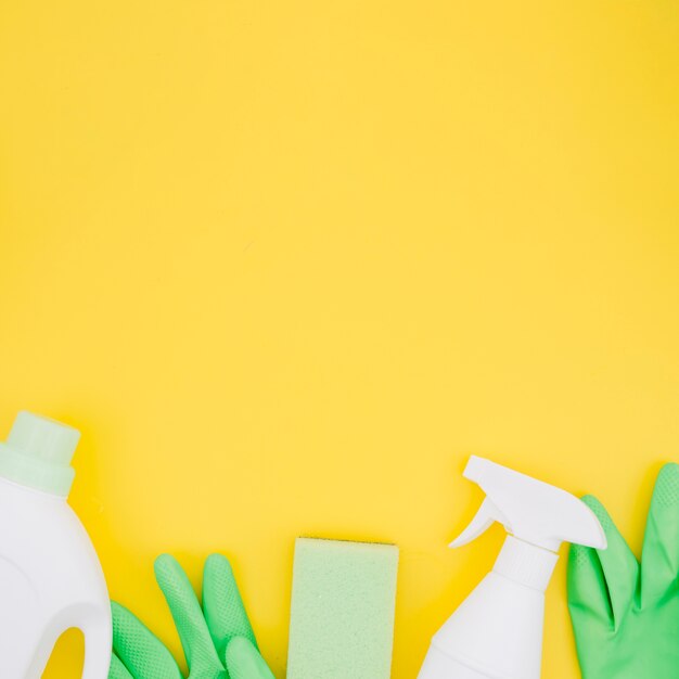 Botellas blancas con guantes verdes y esponja sobre fondo amarillo