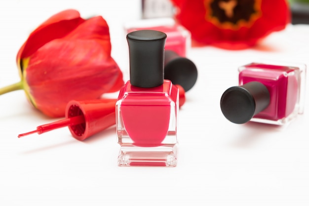 Botellas de esmalte de uñas de color rosa y flores de tulipán sobre fondo blanco.