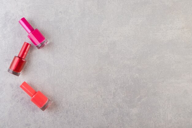 Botellas de esmalte de uñas de colores colocadas sobre una mesa de piedra.