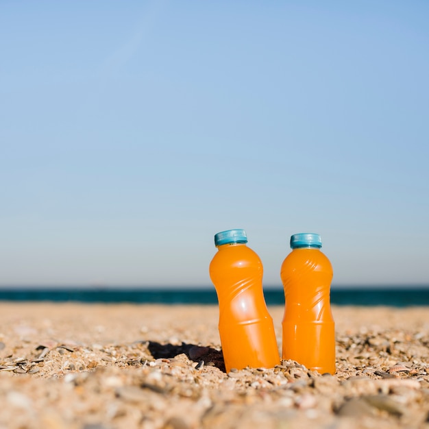 Botellas de jugo saludable en la arena contra el cielo azul en la playa