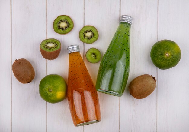 Botellas de jugo de vista superior con mandarinas y kiwi en pared blanca