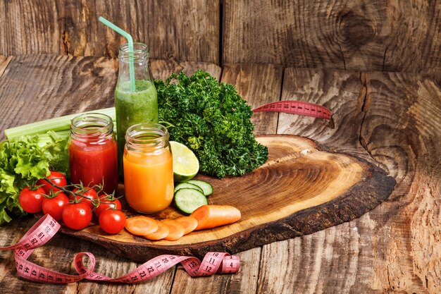 Las botellas con jugos de vegetales frescos en la mesa de madera