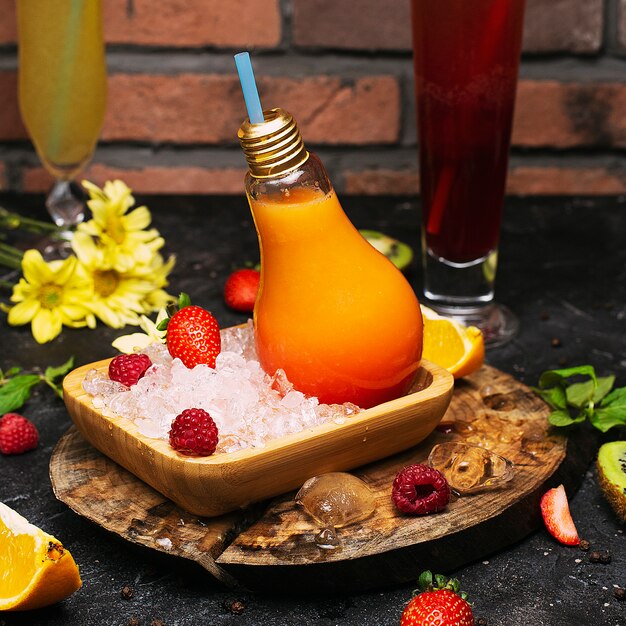 Botellas de vidrio de bombilla con jugo de frutas tropicales de naranja fresco en un plato con cubos de hielo y strawbesrries. Descanso de vacaciones Desintoxicación Desintoxicación Bienestar