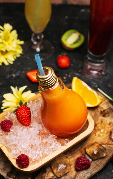 Botellas de vidrio de bombilla con jugo de frutas tropicales de naranja fresco en un plato con cubos de hielo y strawbesrries. Descanso de vacaciones Desintoxicación Desintoxicación Bienestar