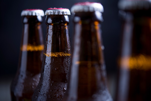 Botellas de vidrio de cerveza con vidrio y hielo sobre fondo oscuro