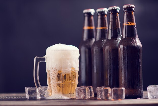 Botellas de vidrio de cerveza con vidrio y hielo sobre fondo oscuro