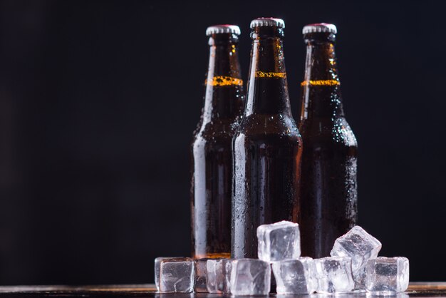 Botellas de vidrio de cerveza con vidrio y hielo sobre fondo oscuro