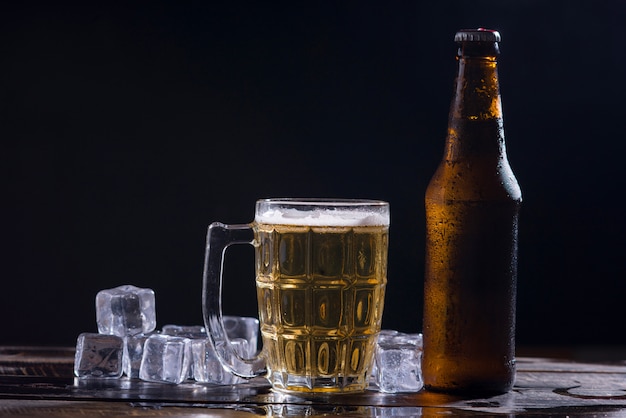 Botellas de vidrio de cerveza con vidrio y hielo sobre fondo oscuro