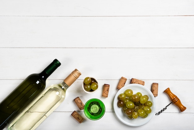 Botellas de vino blanco junto a corchos y uvas.