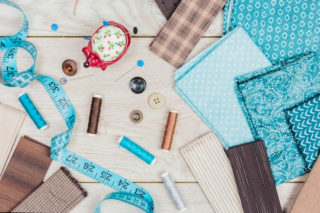 Botones; un conjunto de agujas; Se necesitan carretes de hilo para coser ropa en mesa de madera.