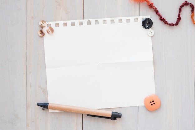 Foto gratuita botones; pluma sobre papel blanco sobre el escritorio de madera