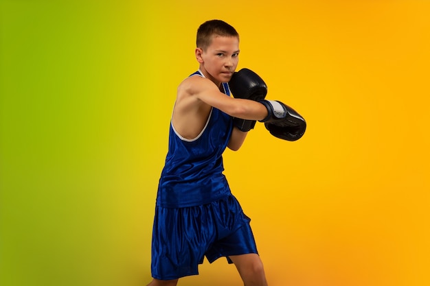 Boxeador adolescente contra el fondo del estudio de neón degradado en movimiento de patadas, boxeo