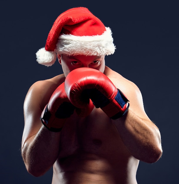 Boxeador de fitness de Navidad con gorro de Papá Noel y guantes rojos de boxeo sobre fondo negro