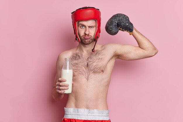 Boxeador de hombre serio con cuerpo delgado usa guantes de boxeo y el sombrero levanta el brazo muestra músculos bebe leche por tener bíceps fuertes demuestra su fuerza y poder. Concepto de deporte y motivación.