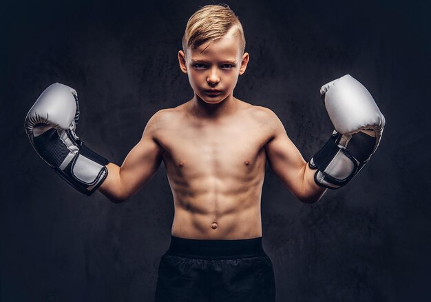 Boxeador joven sin camisa con guantes de boxeo posando en un estudio. Aislado en un fondo de textura oscura.