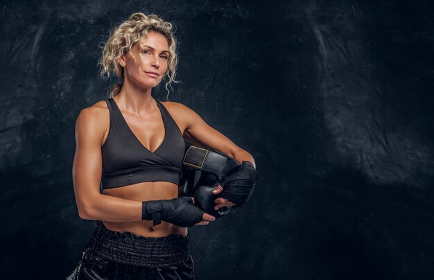 Una boxeadora experimentada posa para una fotógrafa en un estudio fotográfico oscuro con equipo en las manos.