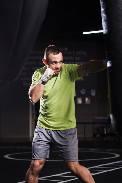 Boxer masculino vistiendo camiseta y pantalones cortos practicando con saco de boxeo