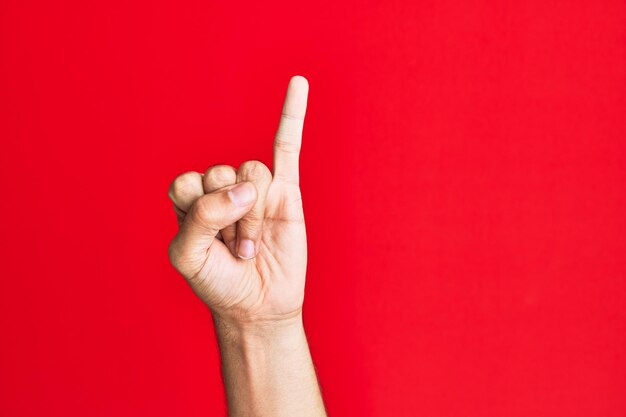 Brazo de un joven blanco caucásico sobre fondo rojo aislado mostrando el dedo meñique como promesa de compromiso número uno