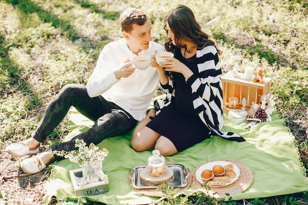 brillante y feliz mujer embarazada sentada en el parque con su marido y bebiendo un té