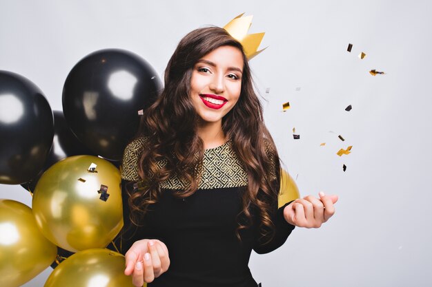 Brillante fiesta de joven alegre en elegante vestido negro de moda y corona amarilla celebrando el año nuevo,