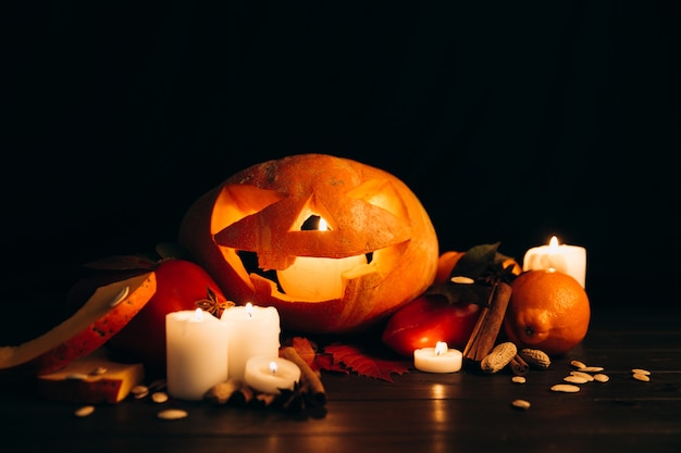 Brillantes velas, canela y hojas caídas frente a la calabaza de Halloween scarry