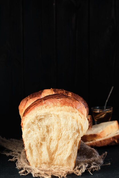 Brioche suave partido por la mitad sobre tabla de madera Miel en un tazón de vidrio en el fondo Concepto horneado de brioche francés dulce tradicional Primer enfoque selectivo los bollos en el marco vertical de la cama de arpillera