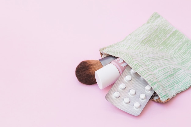 Foto gratuita brocha de maquillaje; botella de barniz de uñas y blister de pastillas blancas dentro de la bolsa de algodón sobre fondo rosa