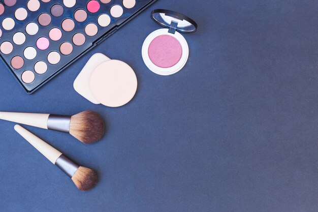 Brocha de maquillaje; esponja; colorete; paleta de sombra de ojos sobre fondo azul