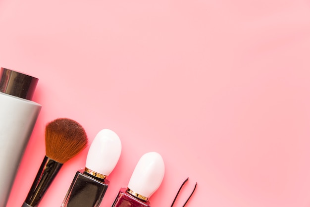 Brocha de maquillaje; Producto cosmético y pinzas sobre fondo rosa.