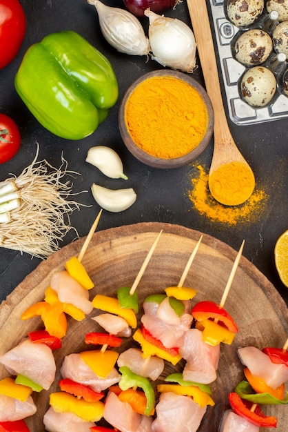 Brochetas de pollo crudo de la mitad superior de la vista en la cúrcuma del tablero de madera natural en un tazón pequeño en la oscuridad