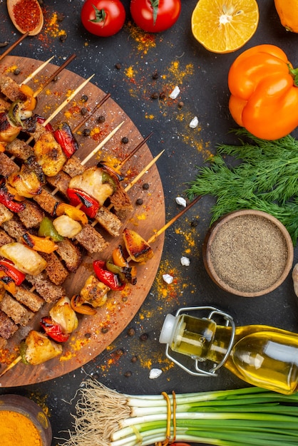 Foto gratuita brochetas de pollo a la parrilla con vista superior sobre tabla de madera y otras cosas en la mesa oscura