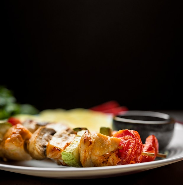 Brochetas de pollo de primer plano en un plato con salsa y patatas fritas