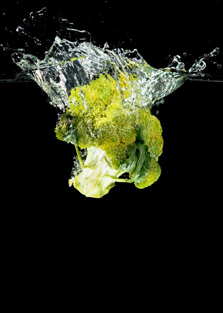 Brócoli cayendo en el agua contra el fondo negro
