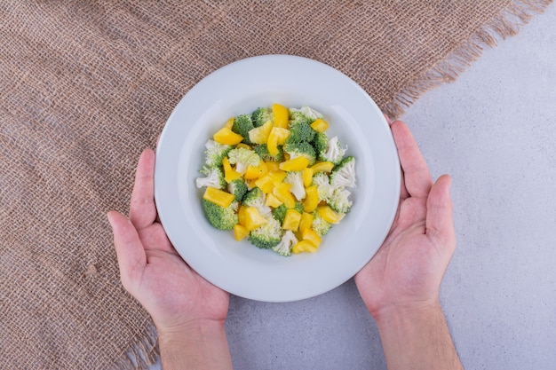 Brócoli fresco, coliflor y pimiento amarillo mezclados en una ensalada sobre fondo de mármol. Foto de alta calidad