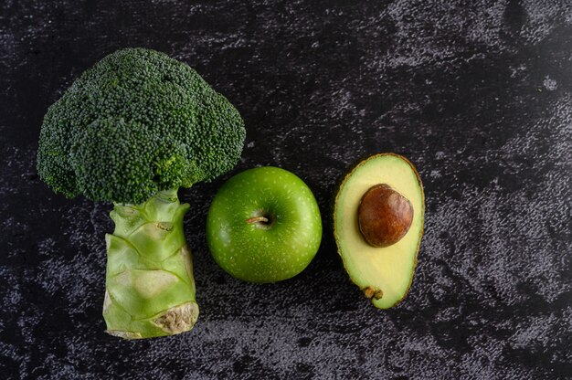 Brócoli, manzana y aguacate en un piso de cemento negro.