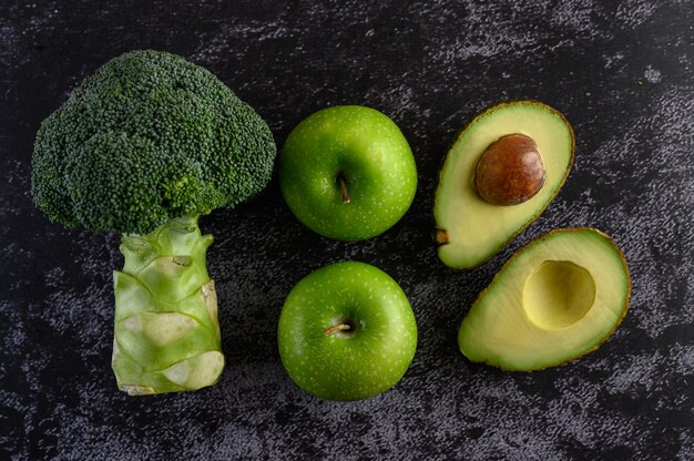 Brócoli, manzana y aguacate en un piso de cemento negro.