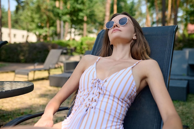 Broncearse. Una linda mujer con gafas de sol tomando el sol y luciendo relajada