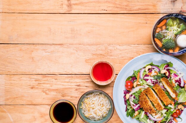 Brotes de soja; sopa; filete; Ensalada con salsas en escritorio de madera