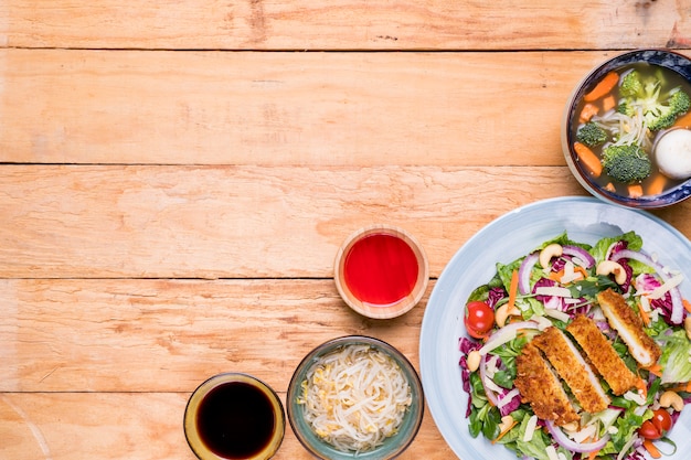 Brotes de soja; sopa; filete; Ensalada con salsas en escritorio de madera