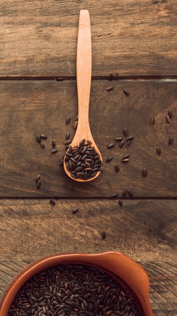 Brown arroz orgánico en cuchara de madera y tazón de fuente en la mesa de madera