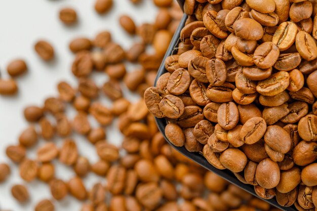 Brown granos de café en una cesta negra en granos dispersos. Vista de ángulo alto.