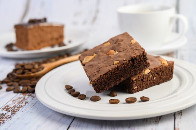 Brownie de chocolate en un plato blanco y granos de café en una cuchara de madera.