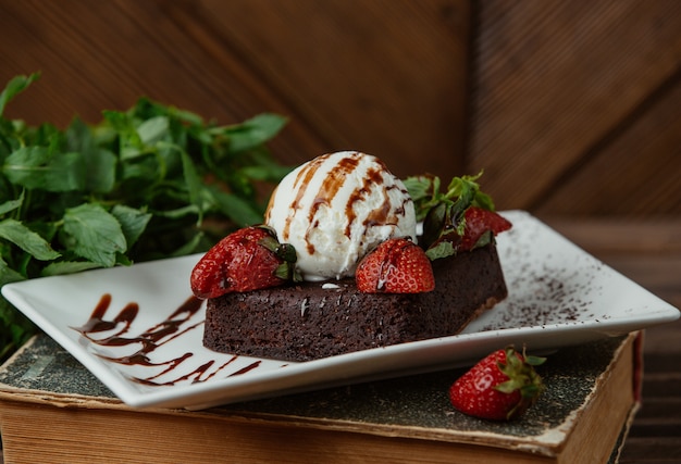 Brownie de chocolate servido con bola de helado de vainilla y fresas