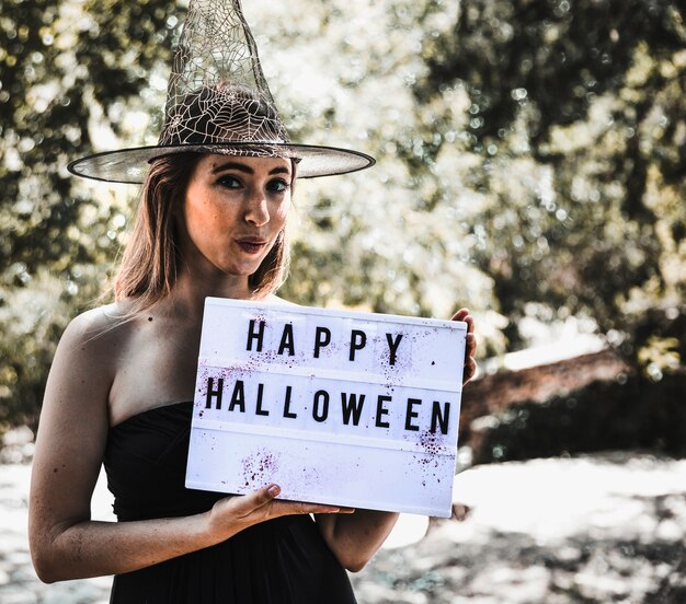 Bruja alegre que sostiene el sigboard con saludo en el bosque soleado