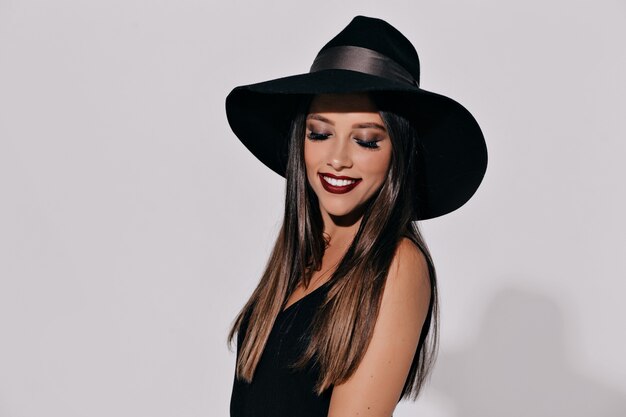 Bruja de Halloween posando en la pared aislada. Hermosa joven eficaz con sombrero de brujas y traje con calabaza. Amplio diseño de arte de fiesta de Halloween.