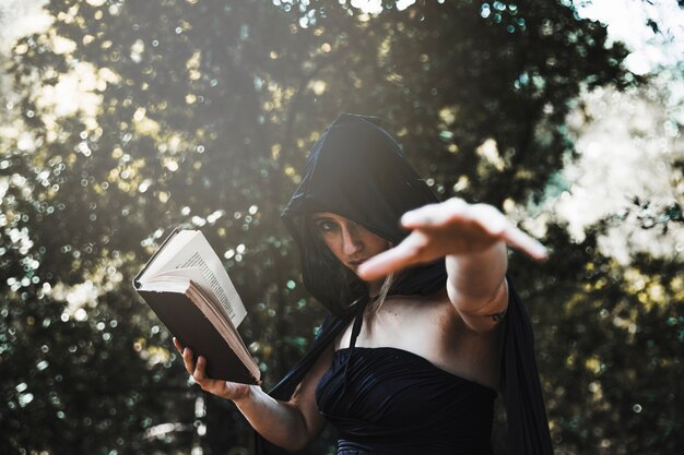 Bruja con libro de hechizos usando magia en bosques iluminados por el sol