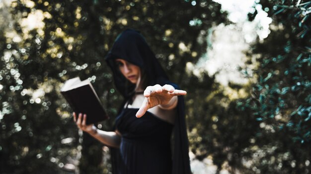 Bruja con libro usando magia en matorral