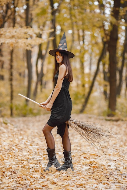 Bruja morena joven en el bosque en Halloween. Chica con vestido negro y sombrero de cono. Bruja sosteniendo cosas de mago.